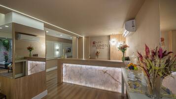 Een hotel receptie met een marmeren balie, houten vloer en een spiegel die het interieur weerkaatst.