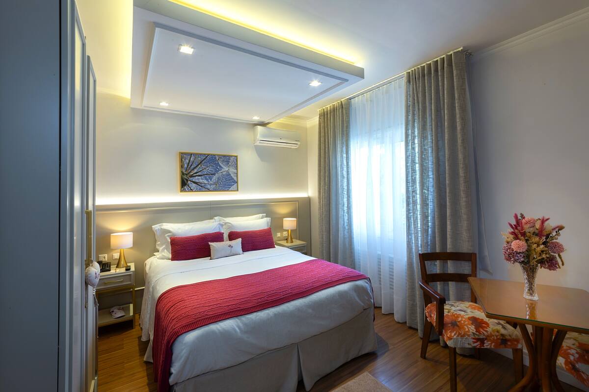 Ein Hotelzimmer mit einem großen Bett, Nachttischen, einem Schreibtisch mit Stuhl und einer Vase mit Blumen.