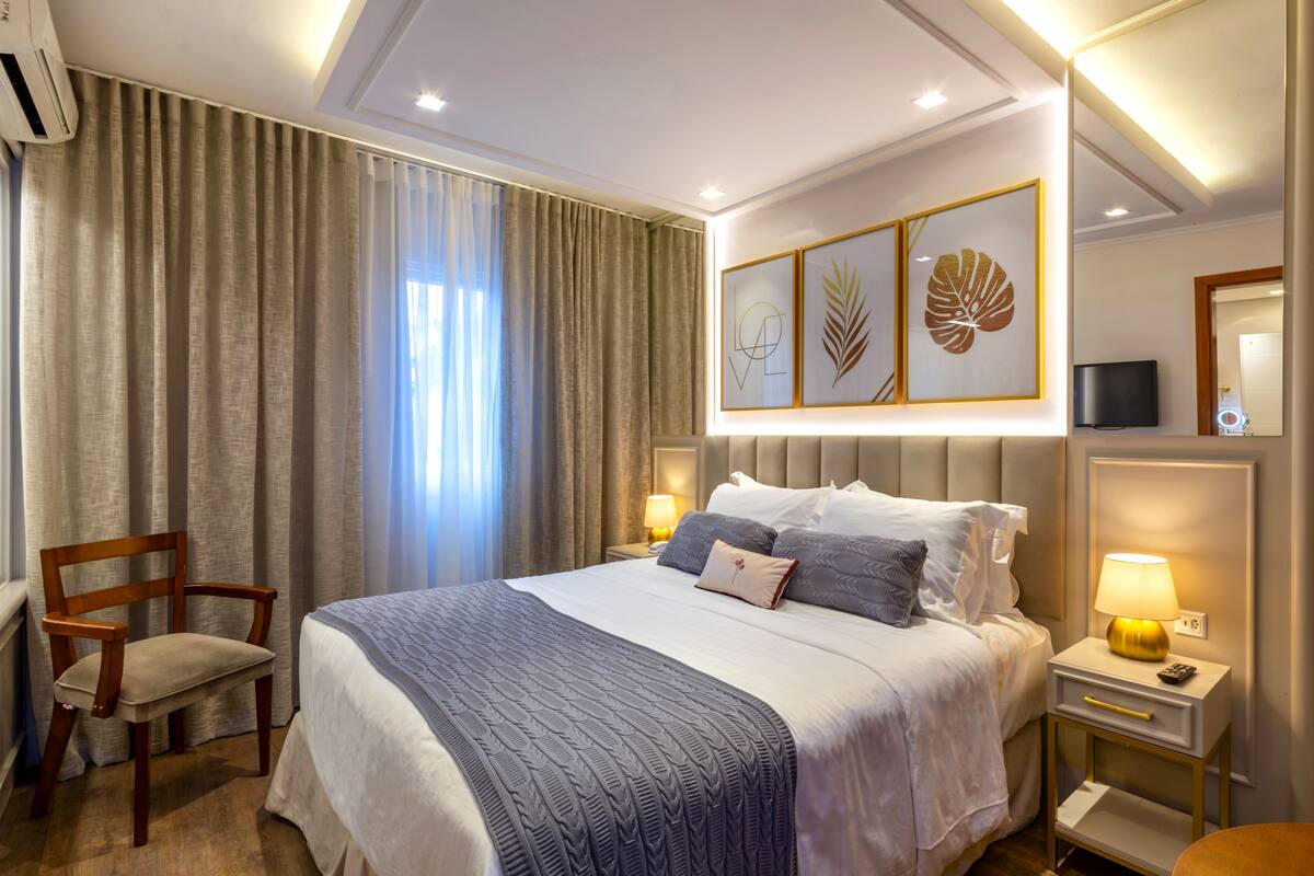 Ein Hotelzimmer mit einem großen Bett, einem Sessel, einem Nachttisch mit Lampe und einem Fernseher.