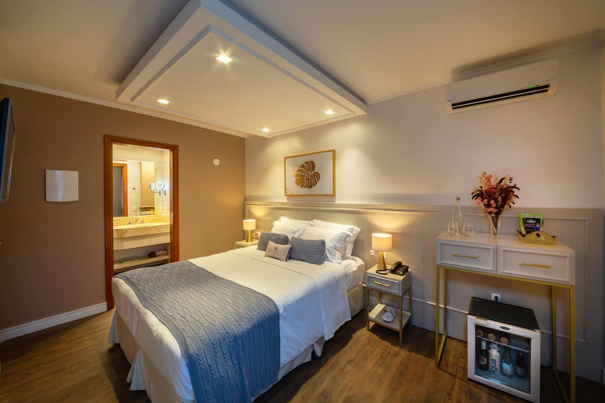 Ein Hotelzimmer mit einem großen Bett, Nachttischen mit Lampen, einem kleinen Kühlschrank und einem Schminktisch mit Spiegel.