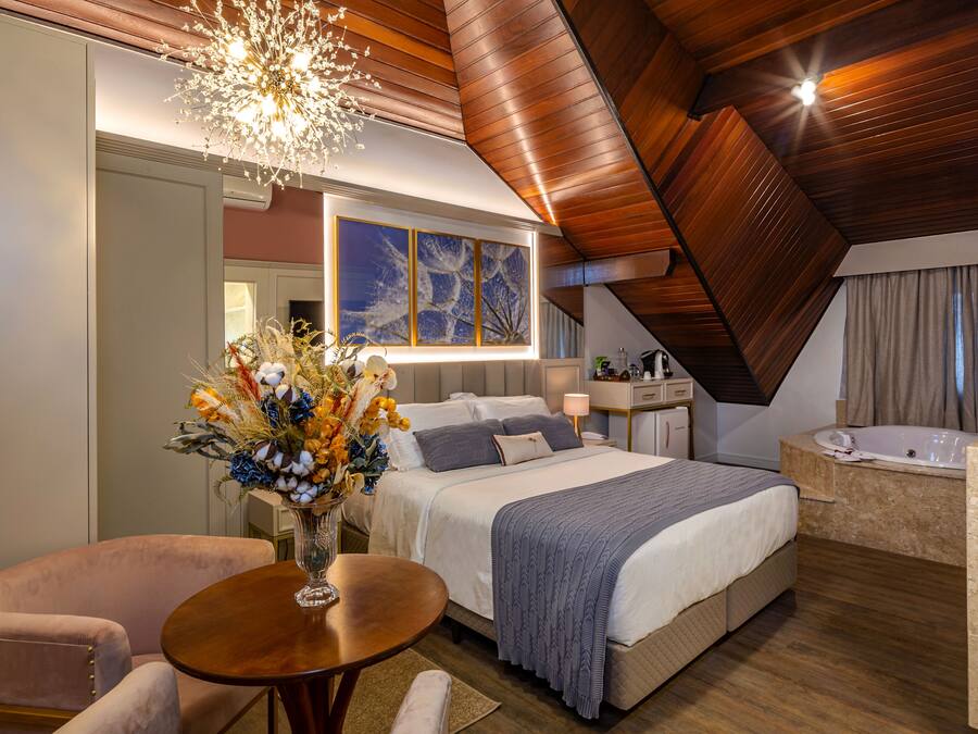 A modern bedroom with a large bed, a sitting area, a vanity, and a bathtub.