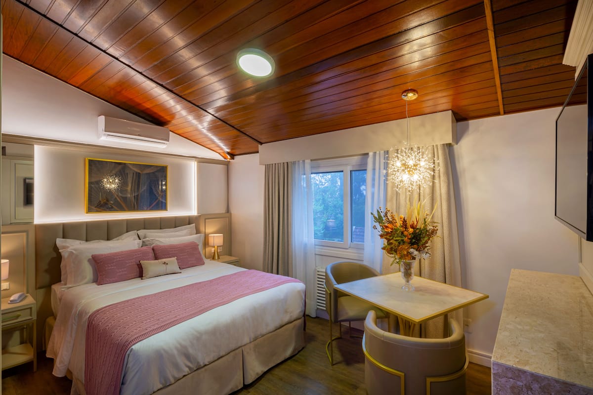 Ein Hotelzimmer mit einem großen Bett, Nachttischen, einem Schreibtisch und einem fensterbepflanzten Fenster.