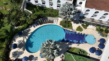 Vista aèria d'un complex turístic amb una gran piscina, gandules i palmeres.