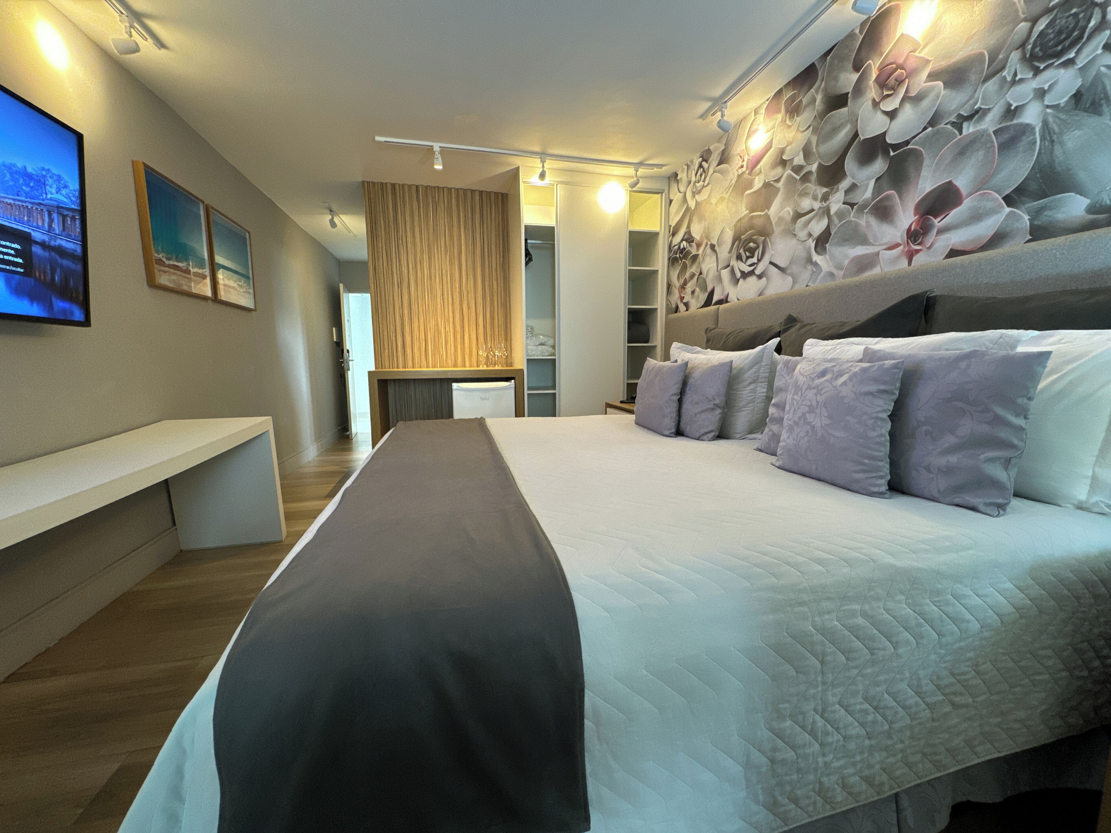 A modern hotel room with a large bed, a flat-screen TV mounted on the wall, and a decorative wall mural.