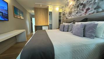 A modern hotel room with a large bed, a flat-screen TV mounted on the wall, and a decorative wall mural.