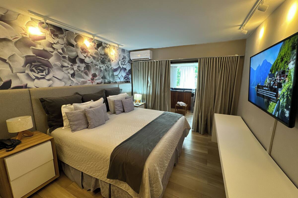 A modern hotel room with a large bed, a TV on the wall, and a decorative floral wall.