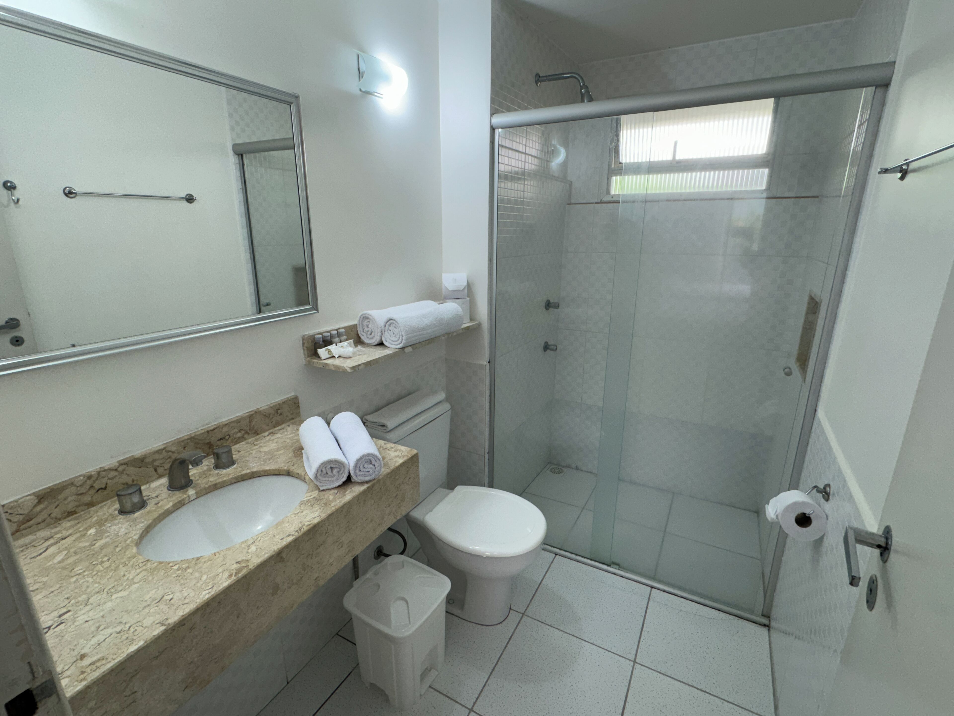 Een badkamer met een marmeren wastafel, een toilet, een douche met glazen wanden en een spiegel.