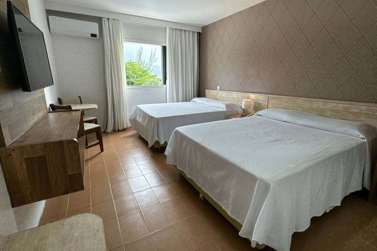 A hotel room with two beds, a desk, a chair, a TV, and a window with curtains.