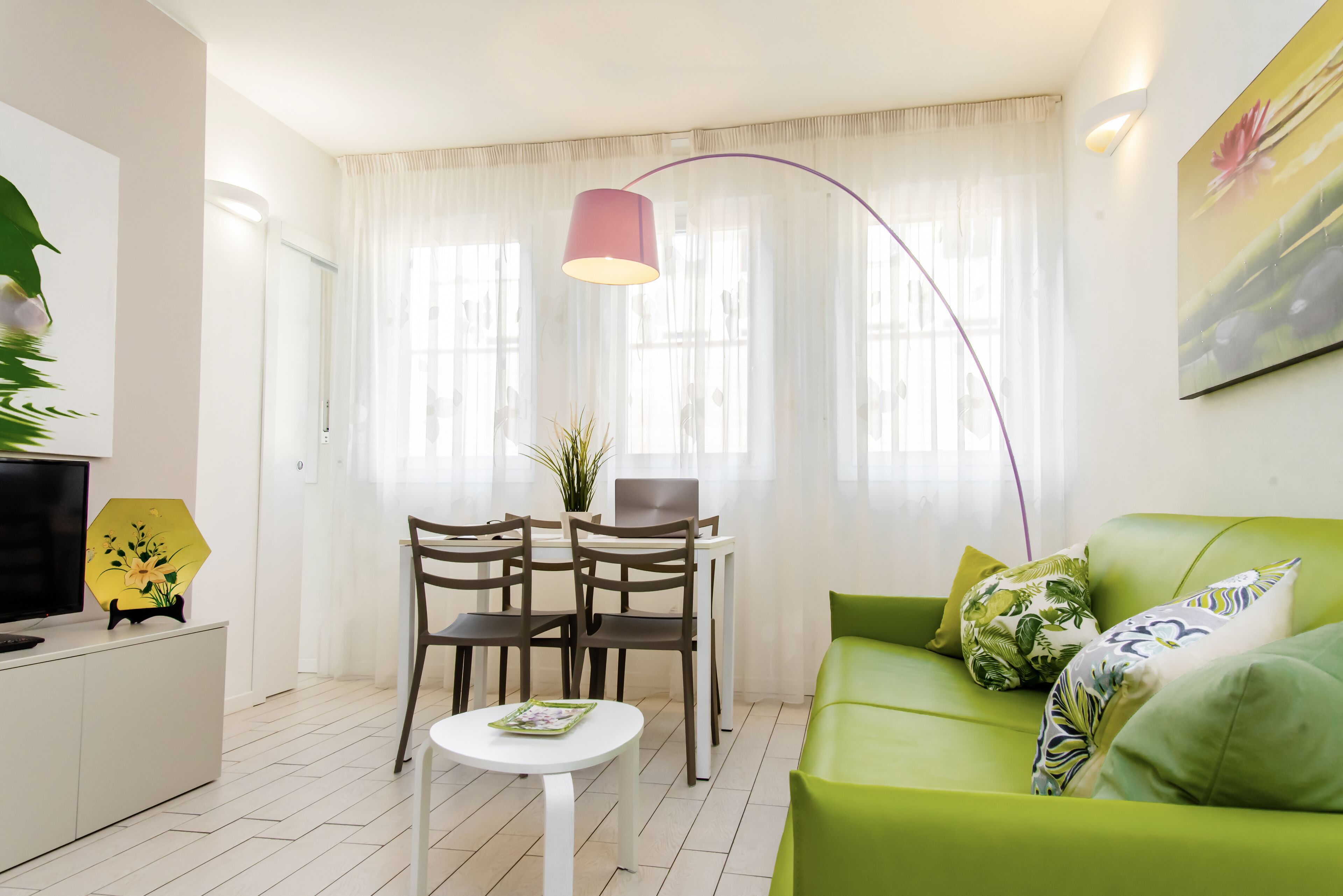 Una sala de estar moderna con un sofá verde, una mesita blanca pequeña y un comedor con dos sillas.