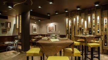 Un restaurante con una mesa larga, sillas amarillas y una estantería con botellas de vino al fondo.