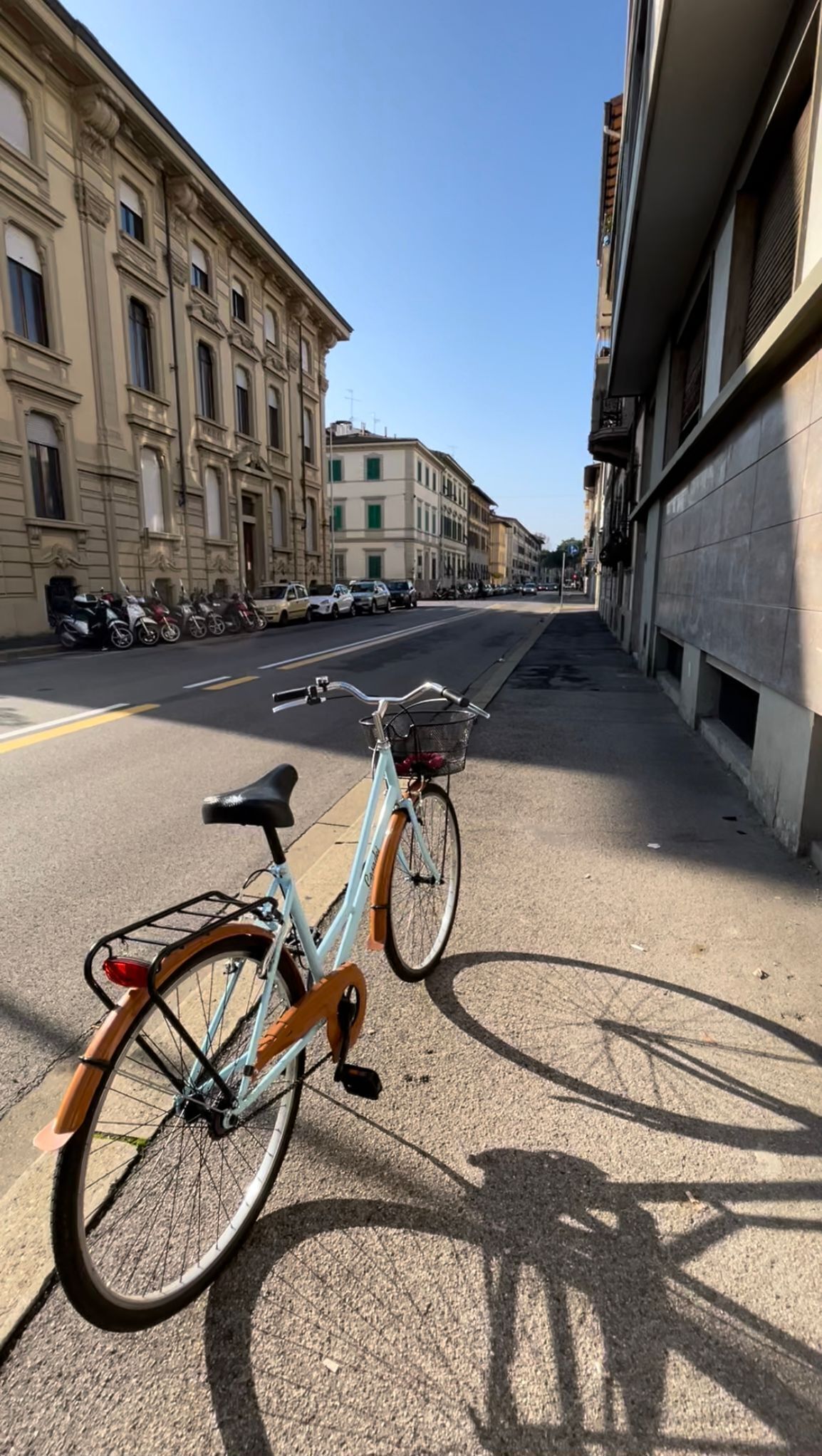 A bicycle parked on a city street with buildings on both sides.