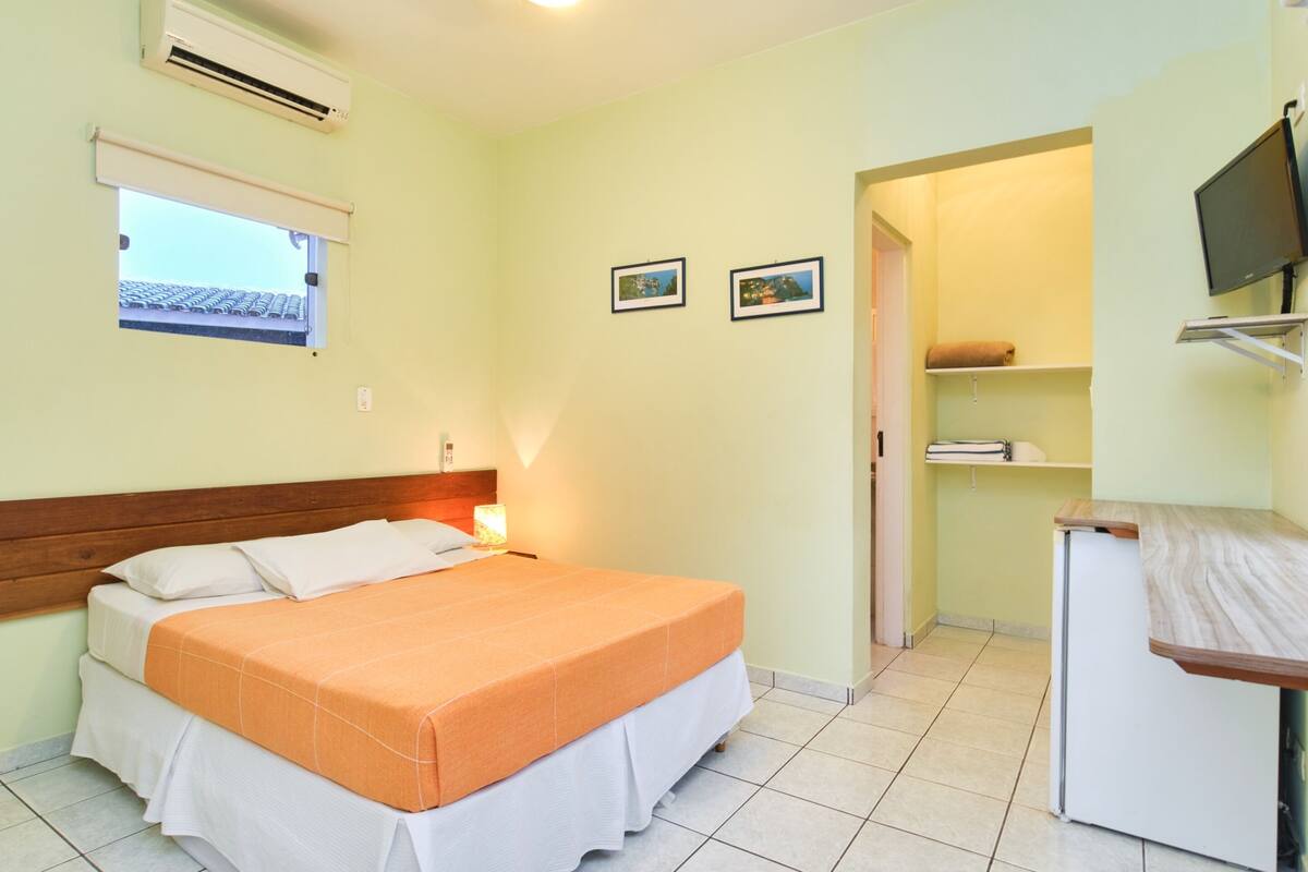 A bedroom with a bed, a desk, a TV, and a window.