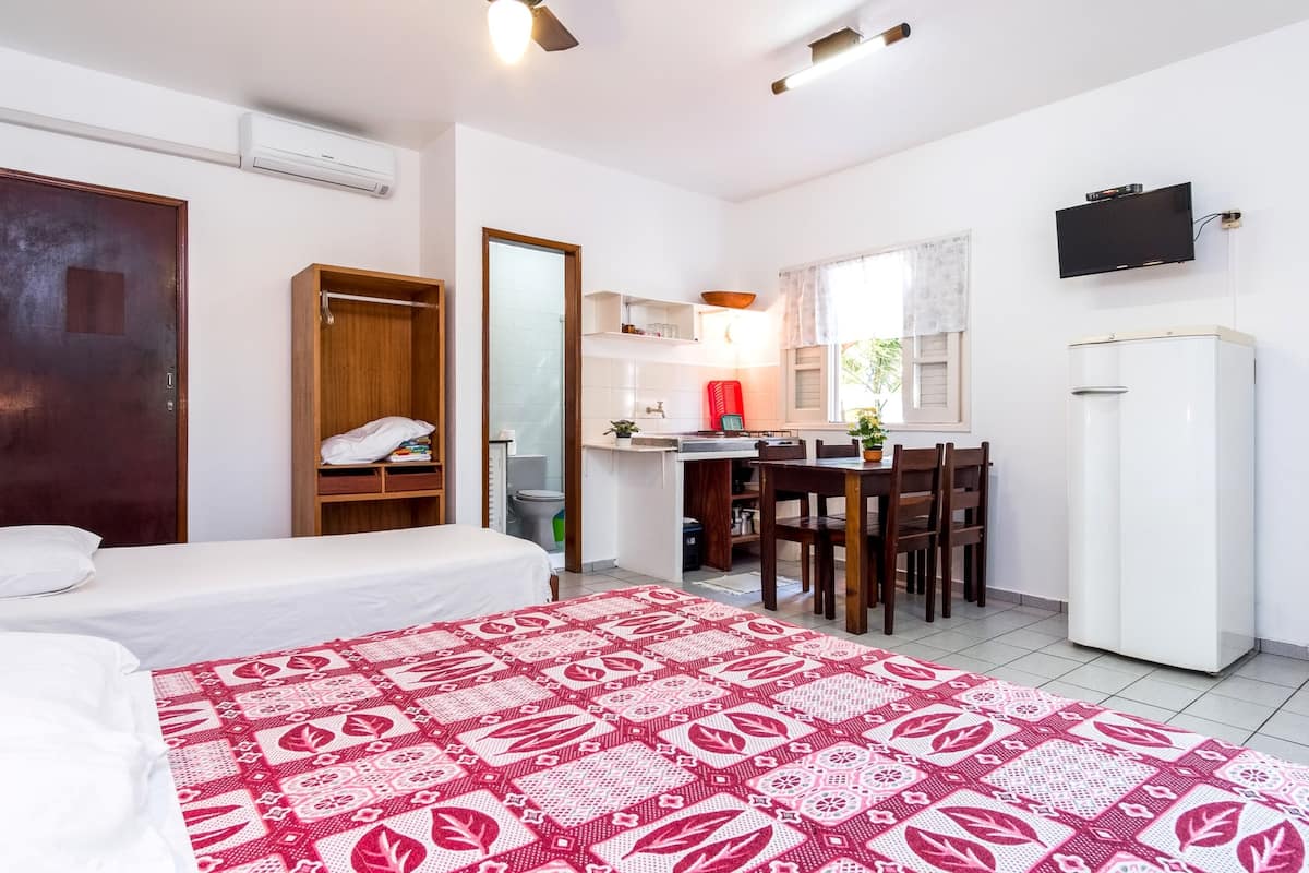 A compact hotel room with a bed, a small kitchenette, a dining area, and a TV mounted on the wall.