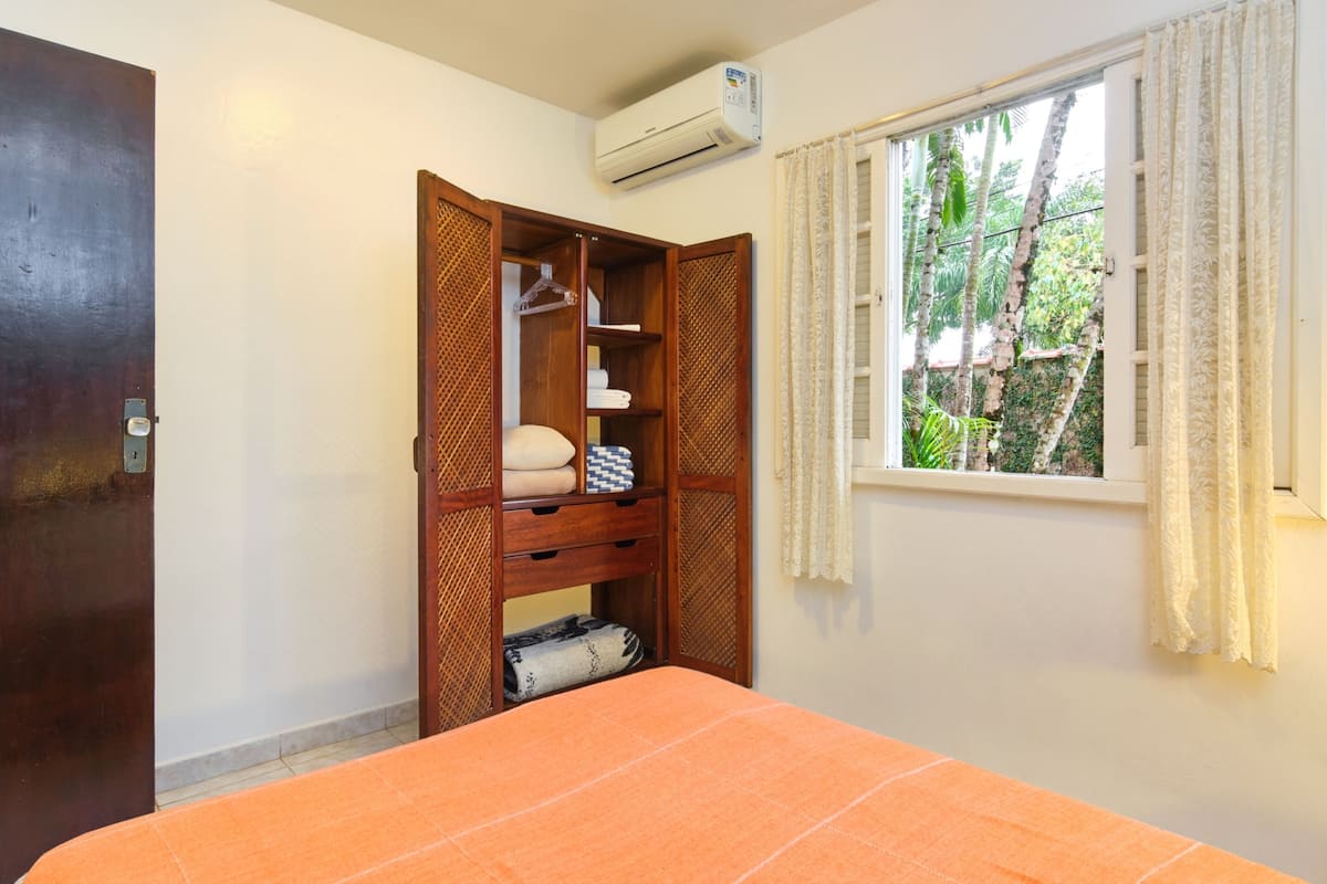 A bedroom with a bed, a wardrobe, a window with curtains, and an air conditioning unit.