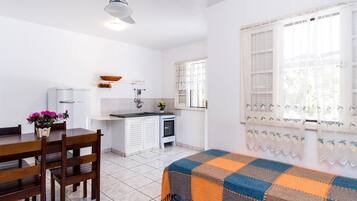 Une cuisine compacte avec des meubles blancs, une table à manger avec des chaises, un petit poêle et une fenêtre ornée de rideaux en dentelle.