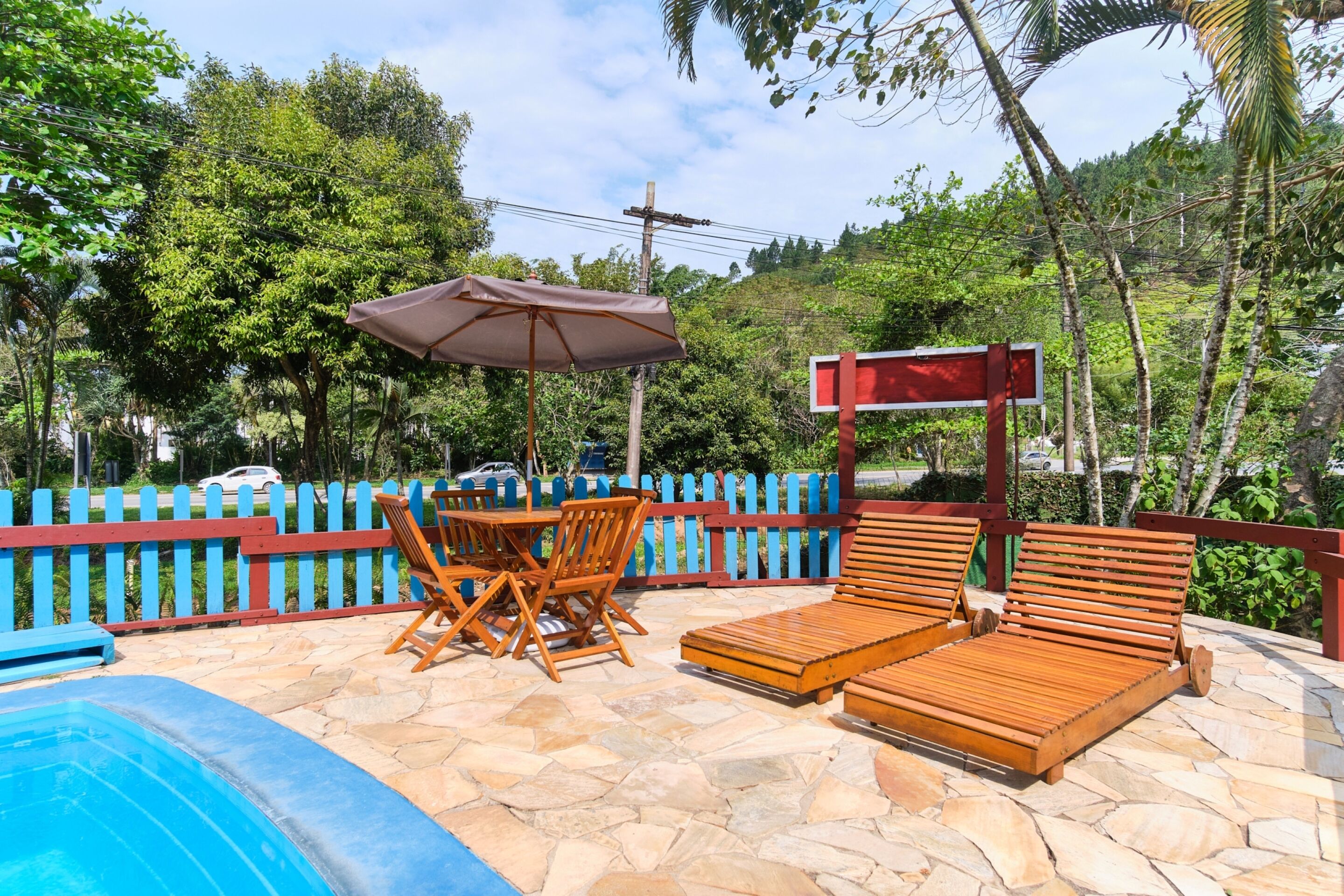 A poolside area with wooden lounge chairs, a table, and an umbrella.
