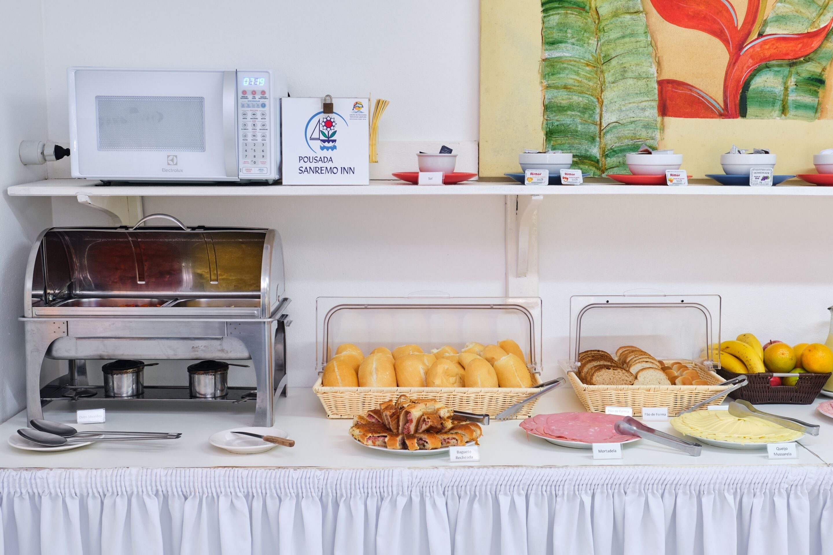 Disposición de bufé con microondas, estación de comidas calientes, pan y diversas opciones para el desayuno.