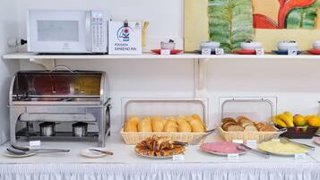 Disposición de bufé con microondas, estación de comidas calientes, pan y diversas opciones para el desayuno.