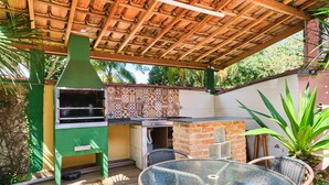 Un patio al aire libre con una mesa de vidrio, sillas de mimbre, una parrilla de ladrillo y una chimenea verde.
