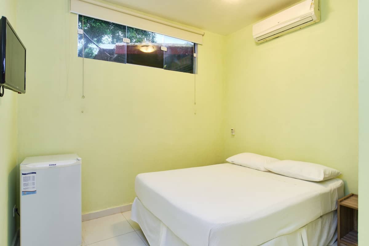 A small, single-bed room with a window, a wall-mounted TV, and a built-in air conditioner.