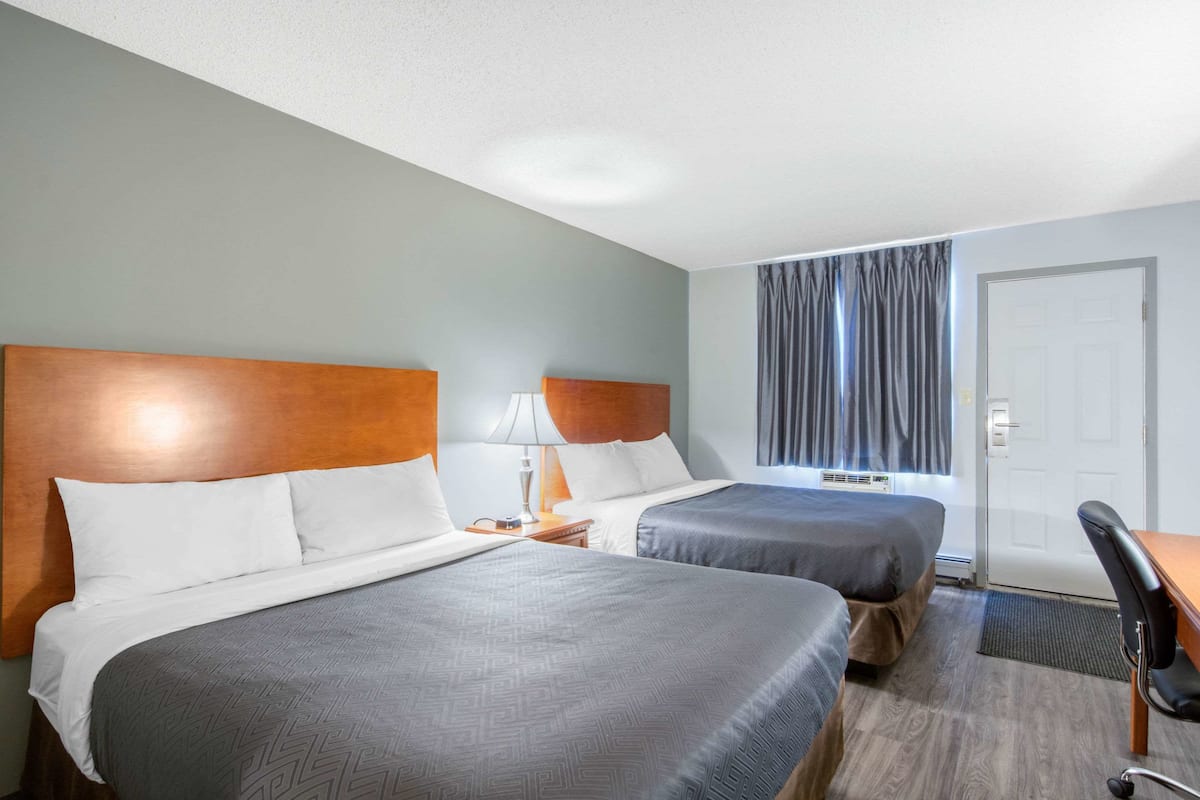 A hotel room with two beds, a desk, and a chair.
