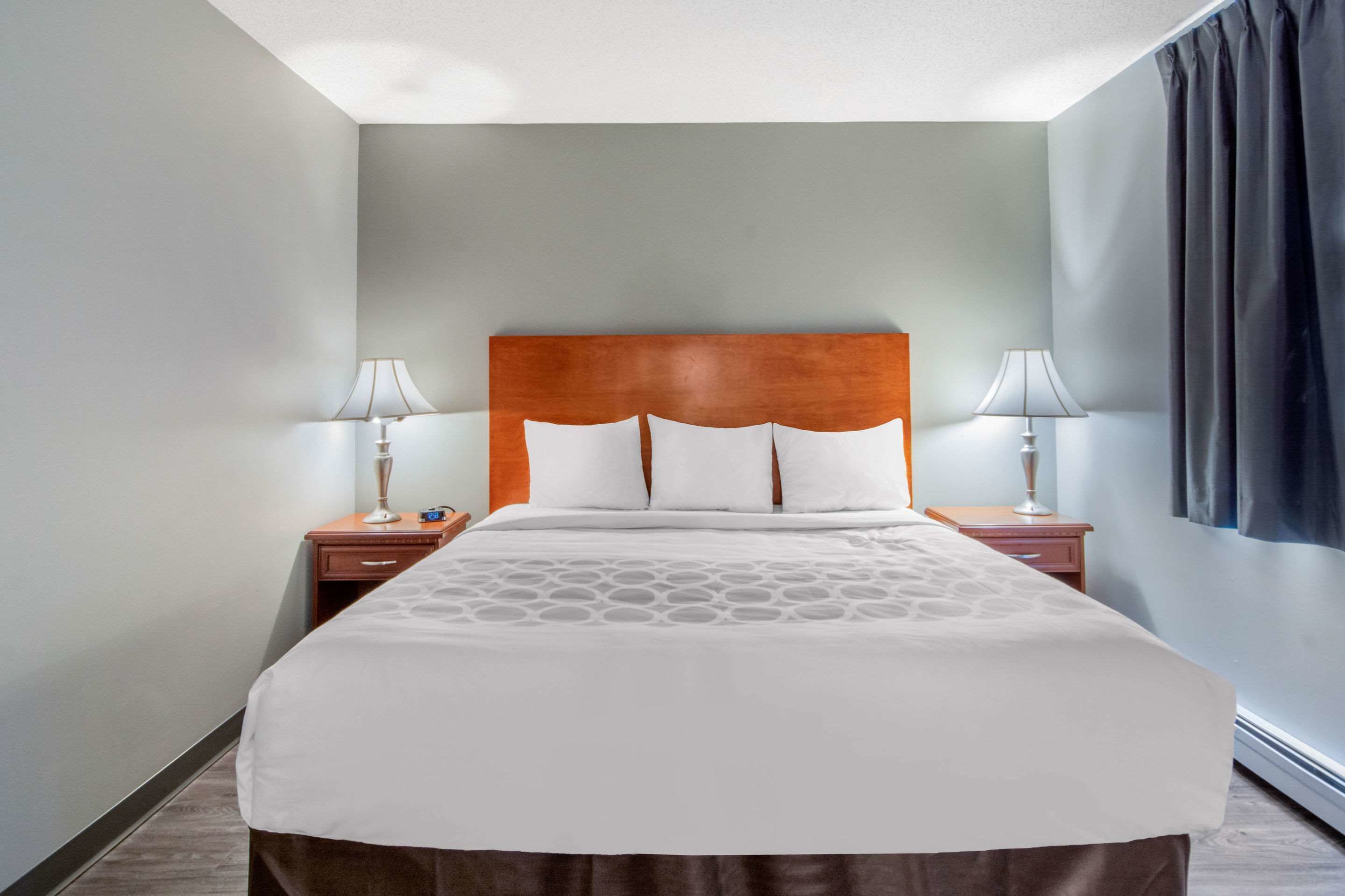 Habitación de hotel con una cama grande, dos mesitas de noche con lámparas y vistas al exterior a través de una ventana con cortinas.