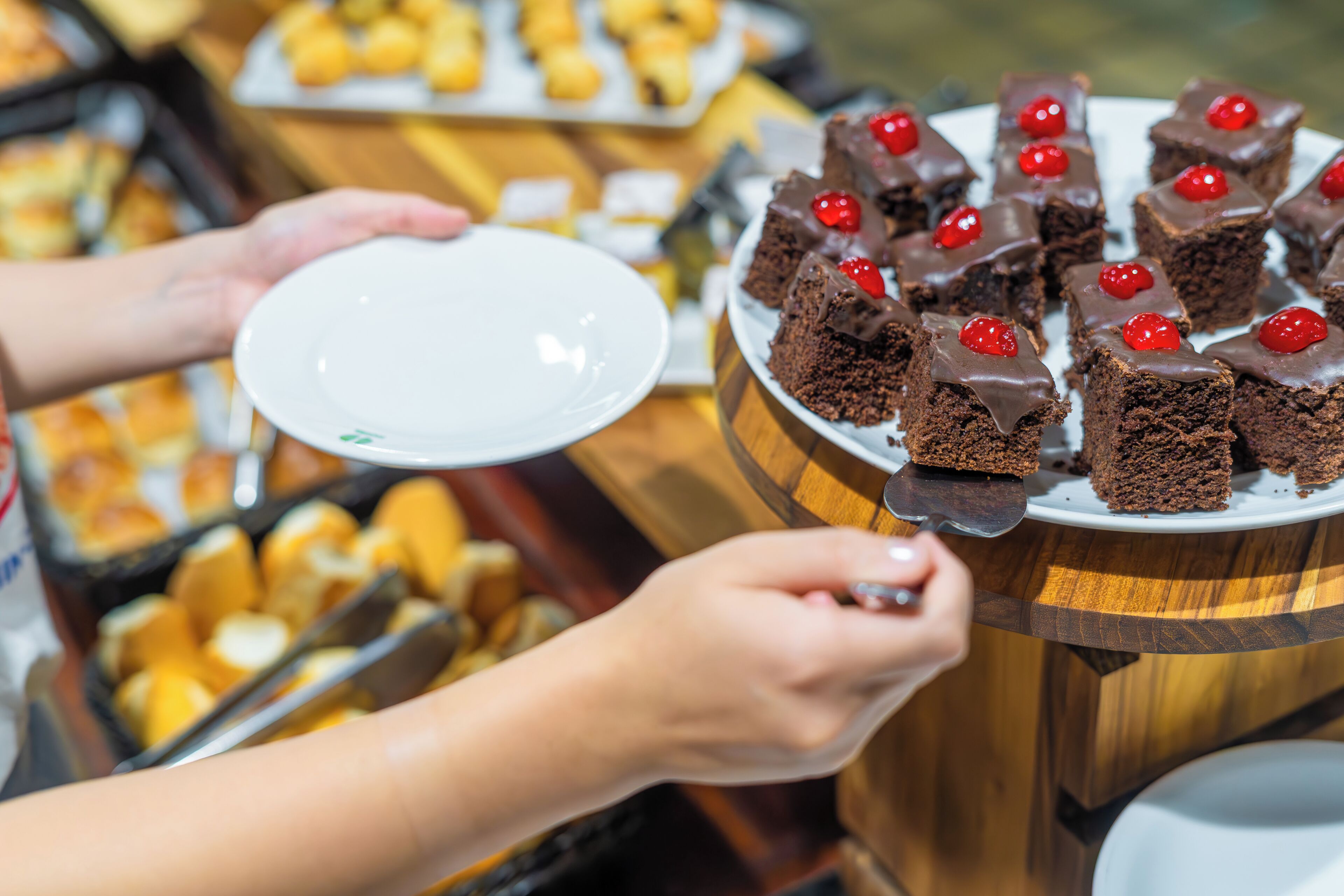 Una persona sirviendo brownies de chocolate con cerezas sobre una mesa de madera.