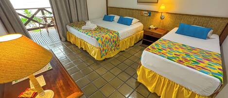 A hotel room with two beds, a wooden table, a lamp, an air conditioning unit, and a balcony with chairs.