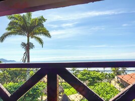A balcony with a view of a palm tree and a coastal landscape.