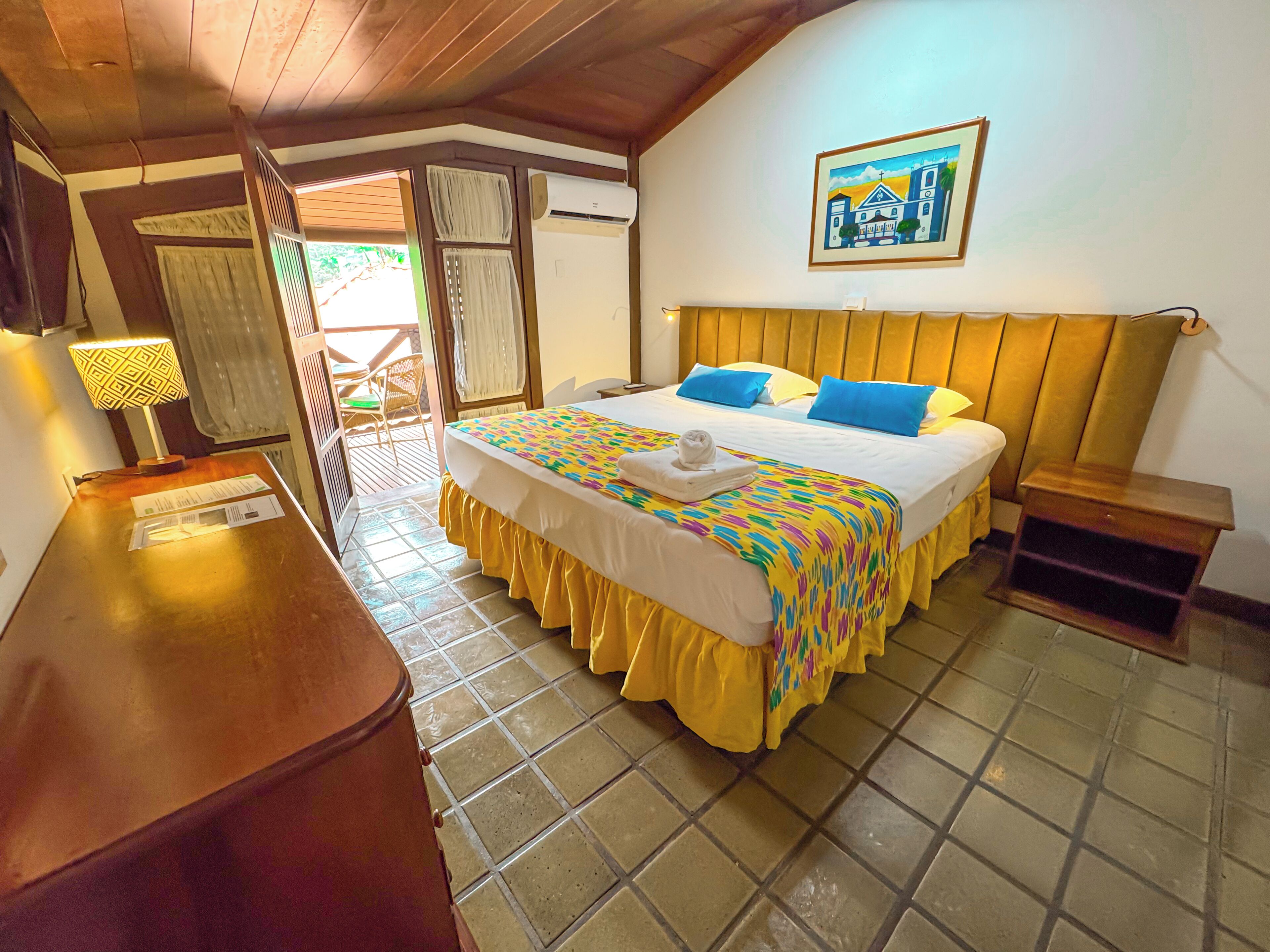 A hotel room with a bed, a wooden desk, a chair, and a picture on the wall.