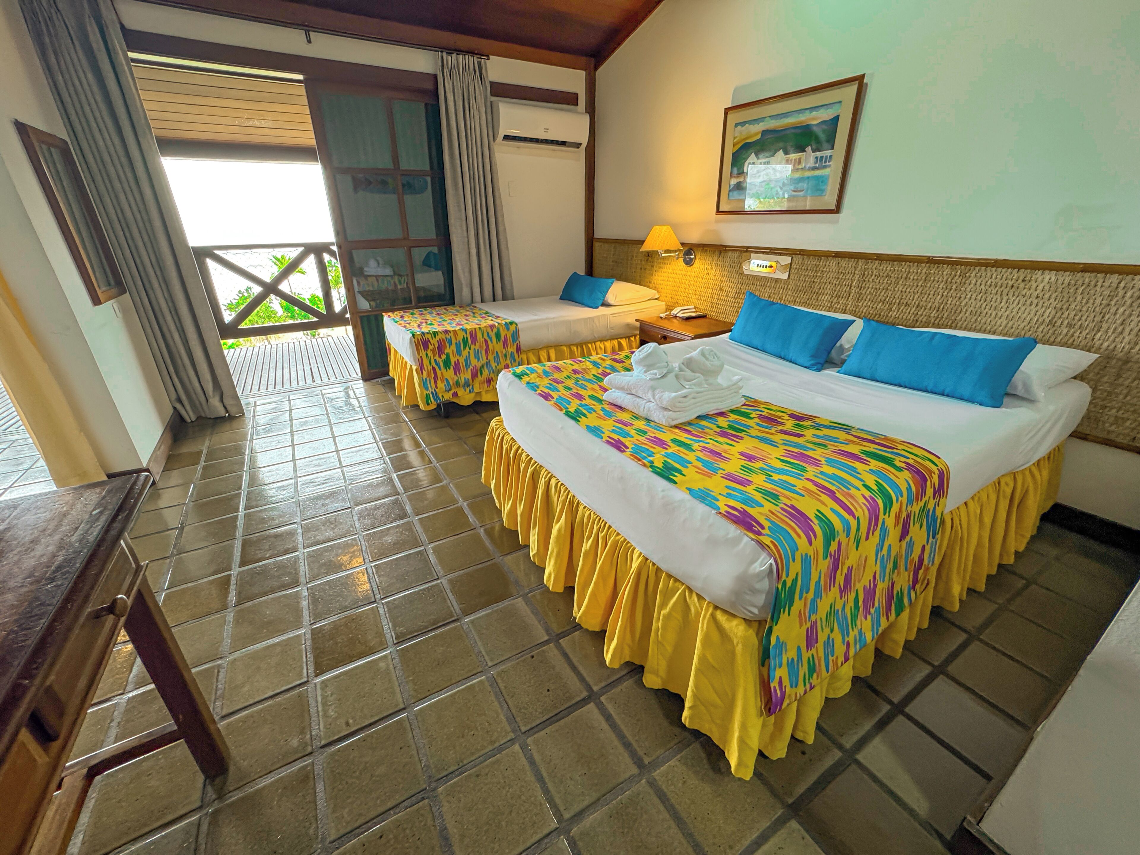 A hotel room with two beds, a balcony, a table, and a painting on the wall.