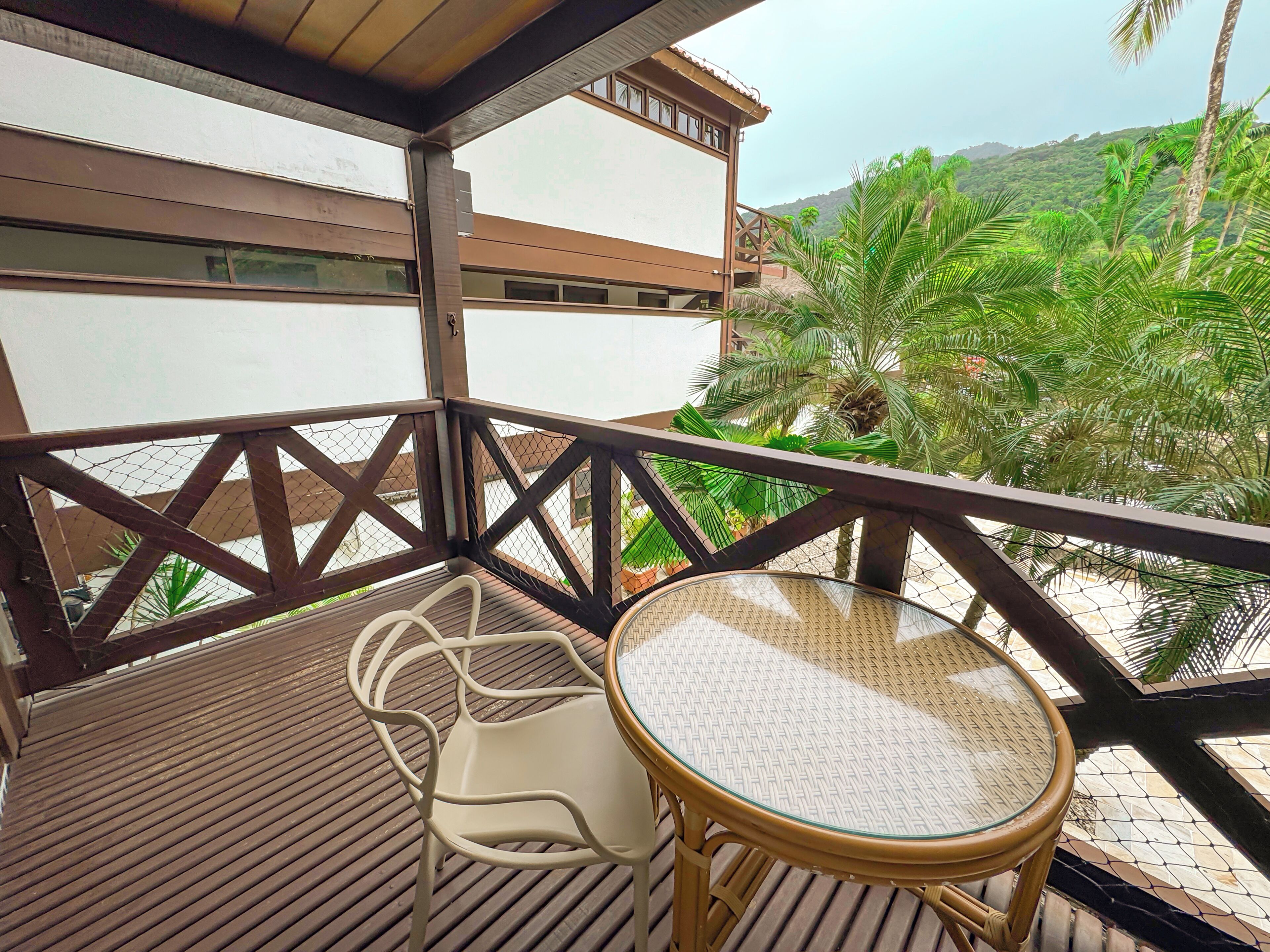 Un balcon avec une table et des chaises, donnant sur un paysage verdoyant et luxuriant et sur un bâtiment.
