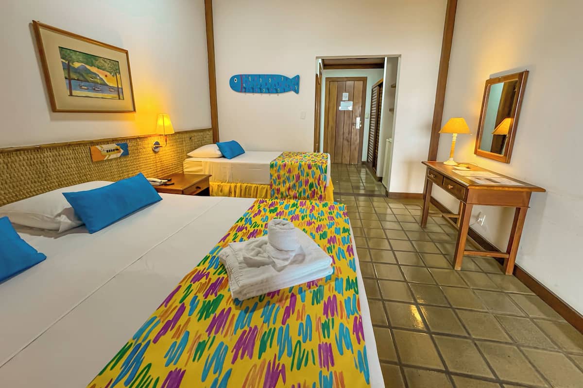 A hotel room with two beds, a desk, a chair, a lamp, a mirror, and a framed picture on the wall.