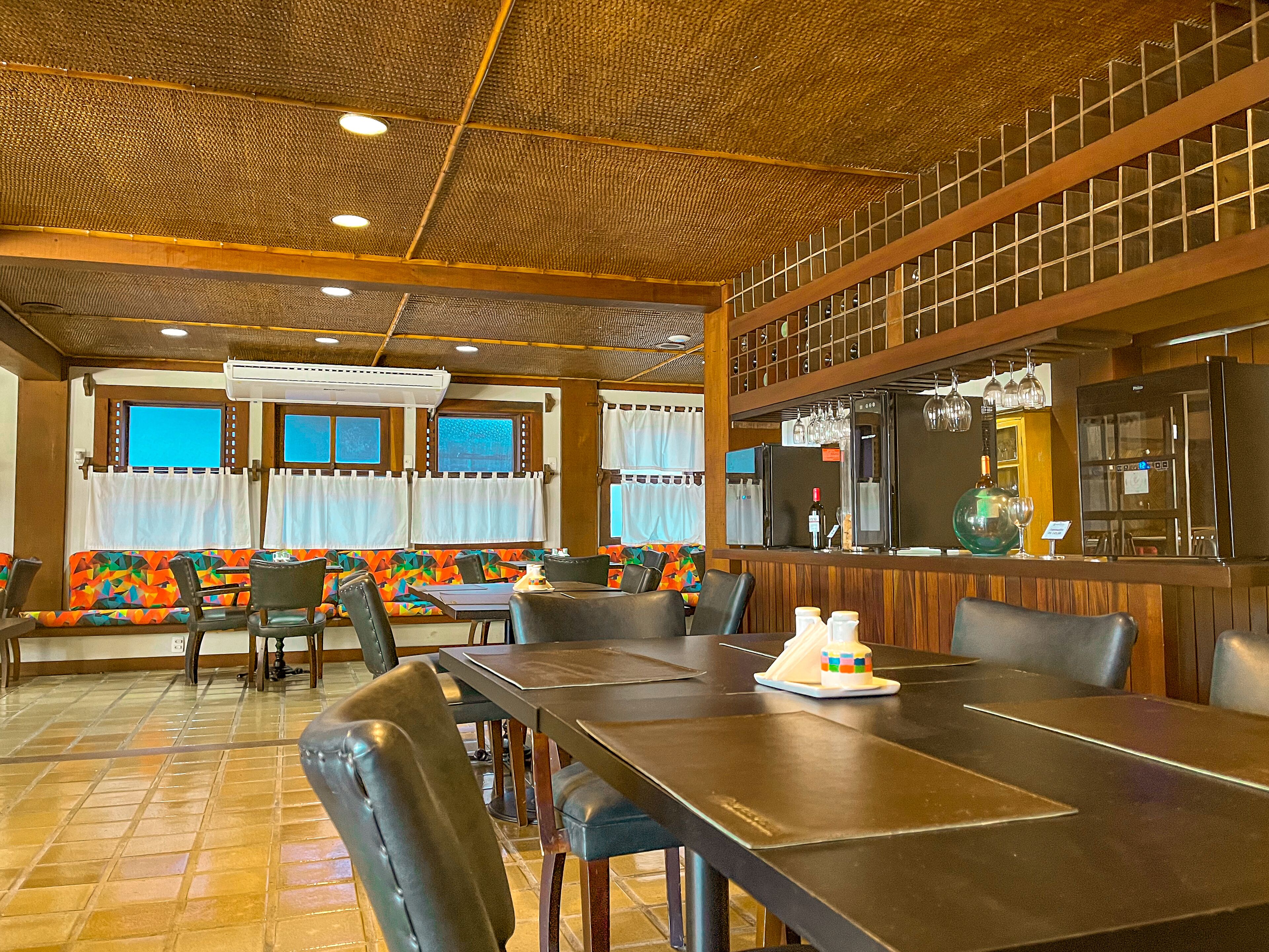 Un restaurante con techo alto, techo decorado y una zona de bar con refrigerador y copas de vino.