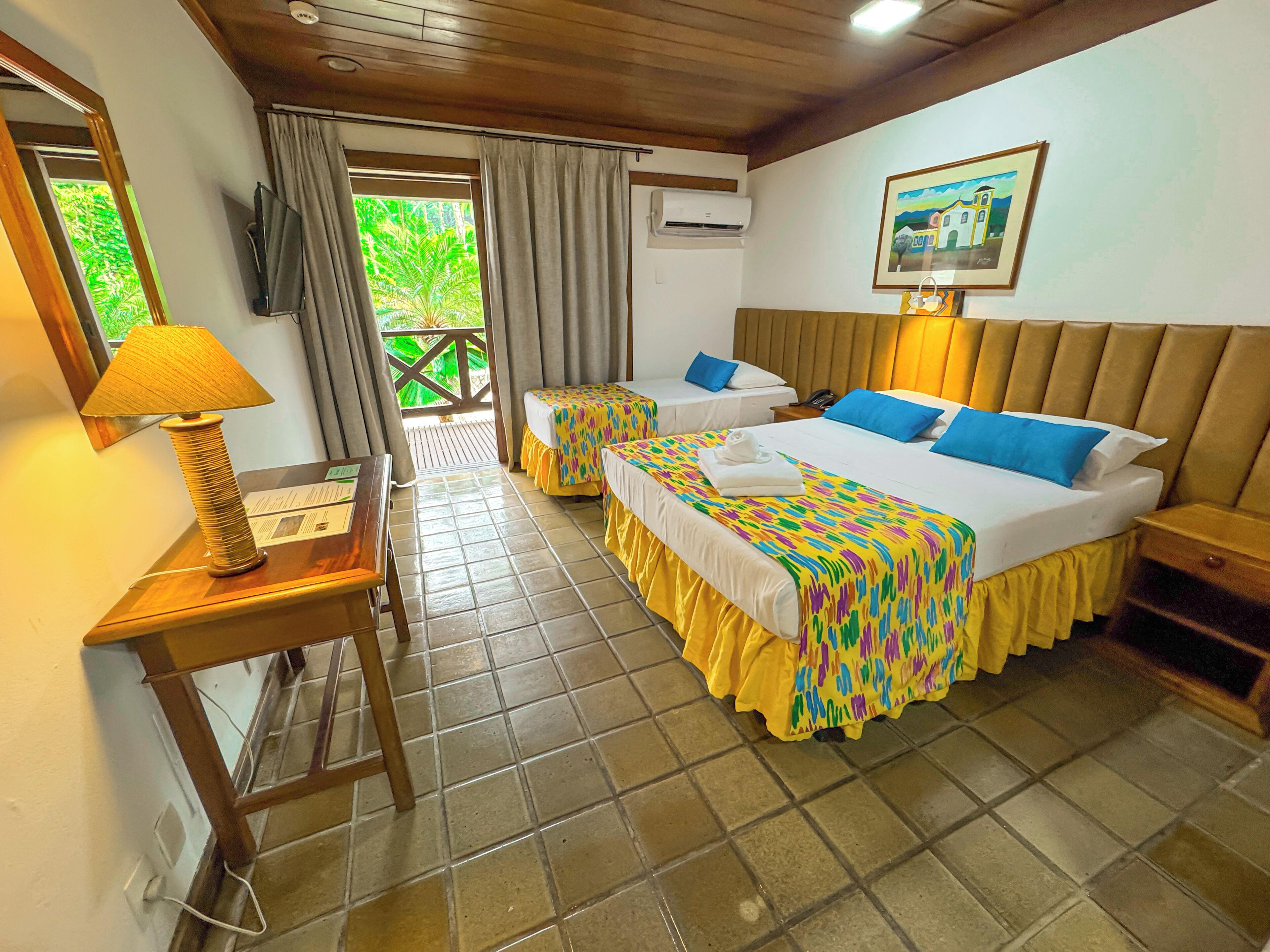 A hotel room with two beds, a desk with a lamp, a TV, and an air conditioning unit.