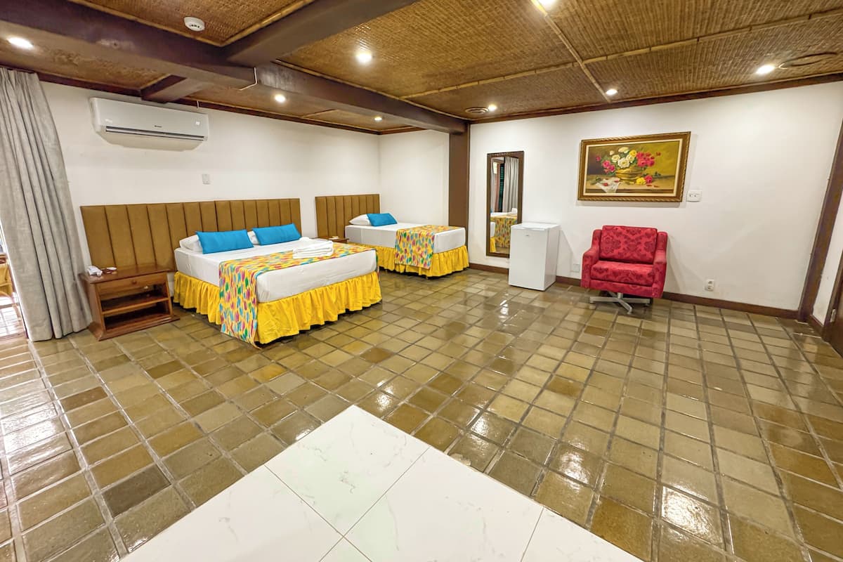 A hotel room with two beds, a red chair, a small table, and a mirror.