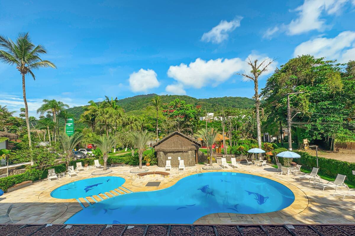 A hotel with a large pool, palm trees, and a mountainous backdrop.