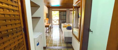A narrow hallway with a tiled floor, a wooden door on the left, and a bed with a headboard and curtains in the center.
