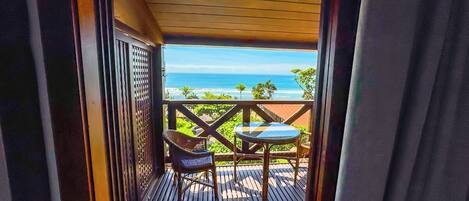 A wooden deck with a table and chairs, overlooking a beach and ocean.