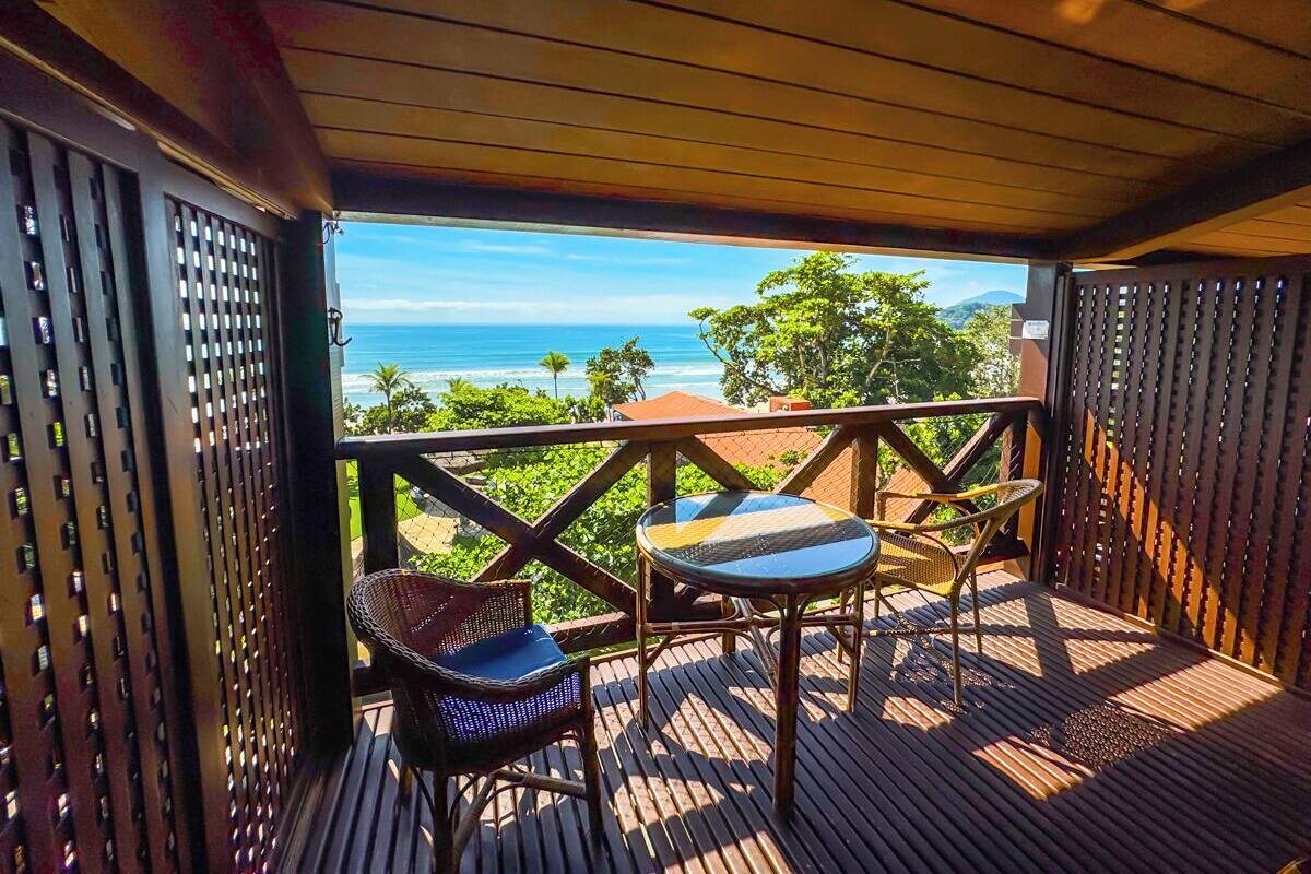 A wooden deck with two wicker chairs and a small table, overlooking a scenic ocean view.