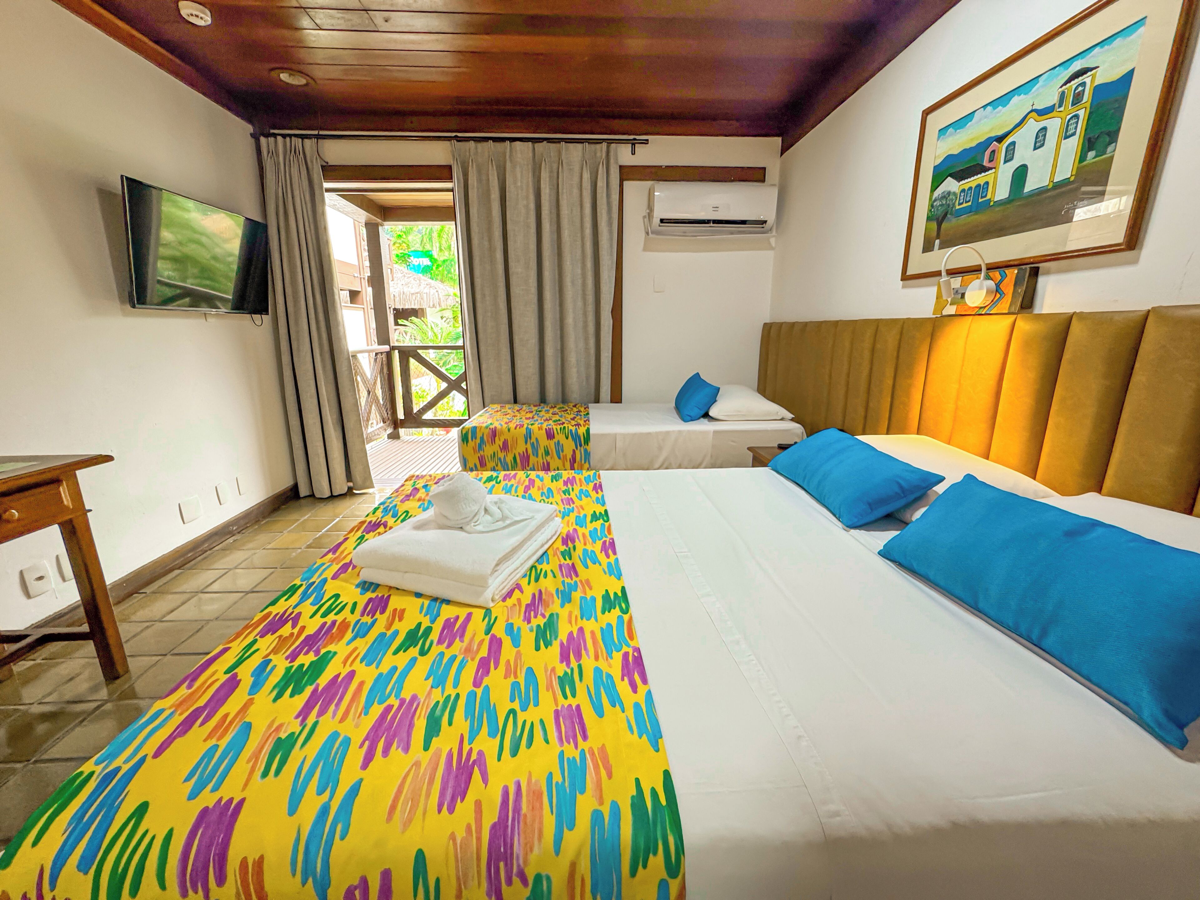 Quarto de hotel com duas camas, televisão, aparelho de ar condicionado e um quadro na parede.