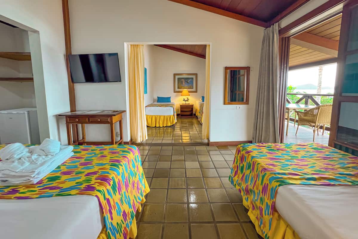 A hotel room with two beds, a desk, a TV, and a view of the outdoors.