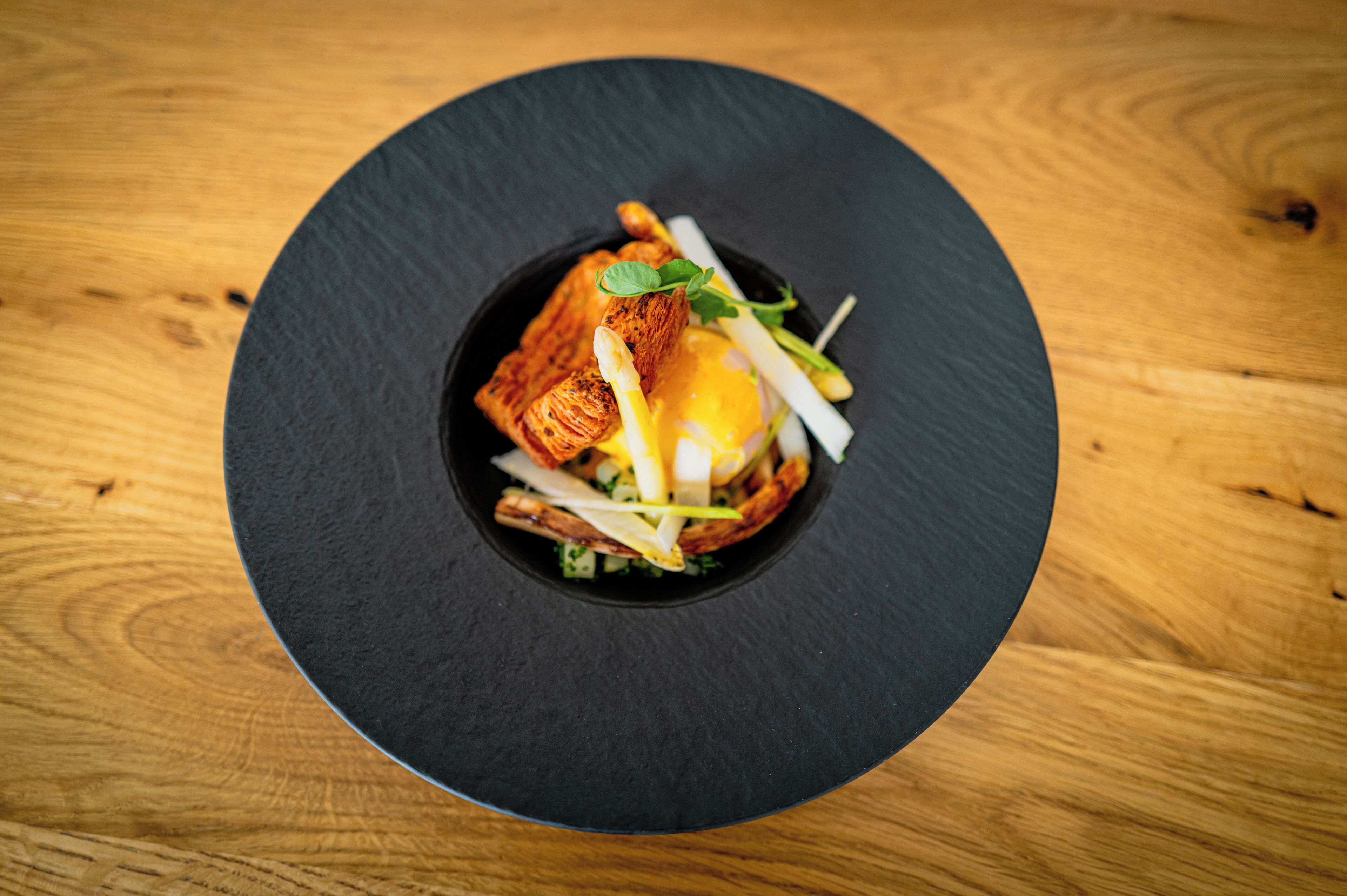 A black plate with a food dish on a wooden table.