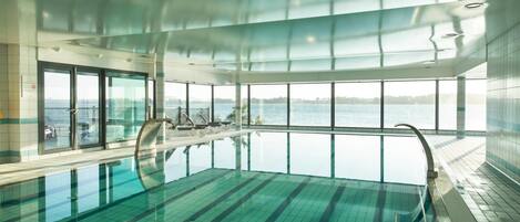 Una piscina interior con vistas claras al mar, ventanas amplias y un diseño moderno.