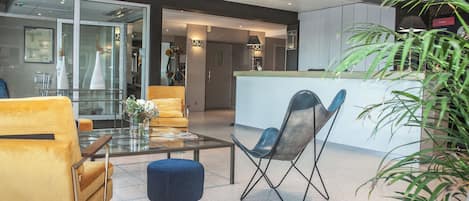 Un área de estar moderna con una mesa de centro de vidrio, un sofá amarillo, un reposapiés azul y una silla plegable negra.