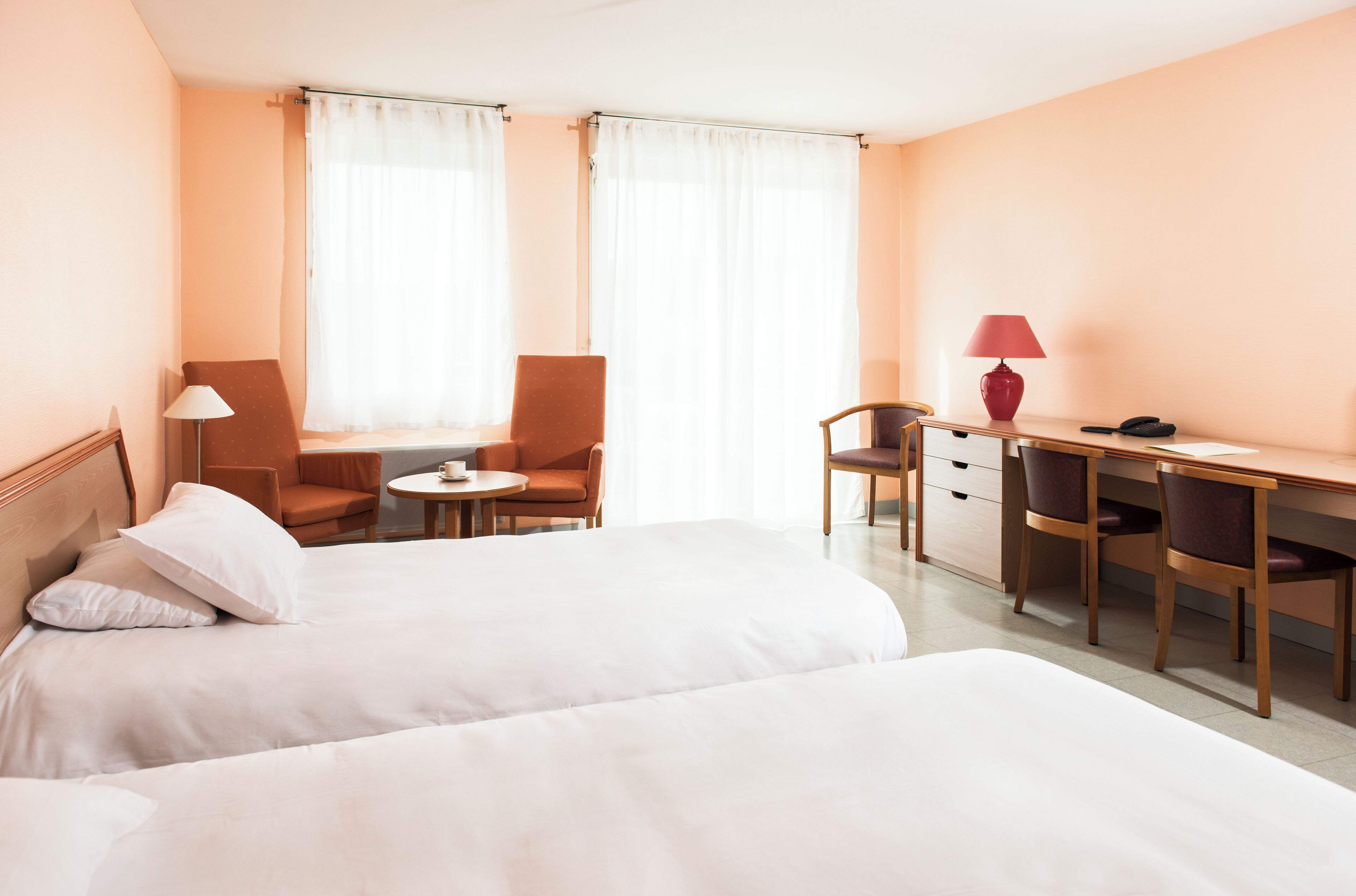 Habitación de hotel con dos camas, un escritorio, una silla, una lámpara y una ventana con cortinas.