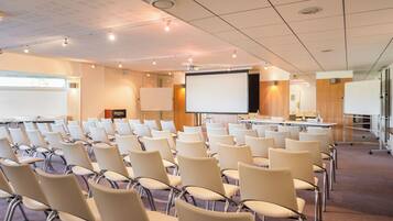 Ein Konferenzraum mit Stuhlreihen, einer Projektionsleinwand und einer Whiteboard.