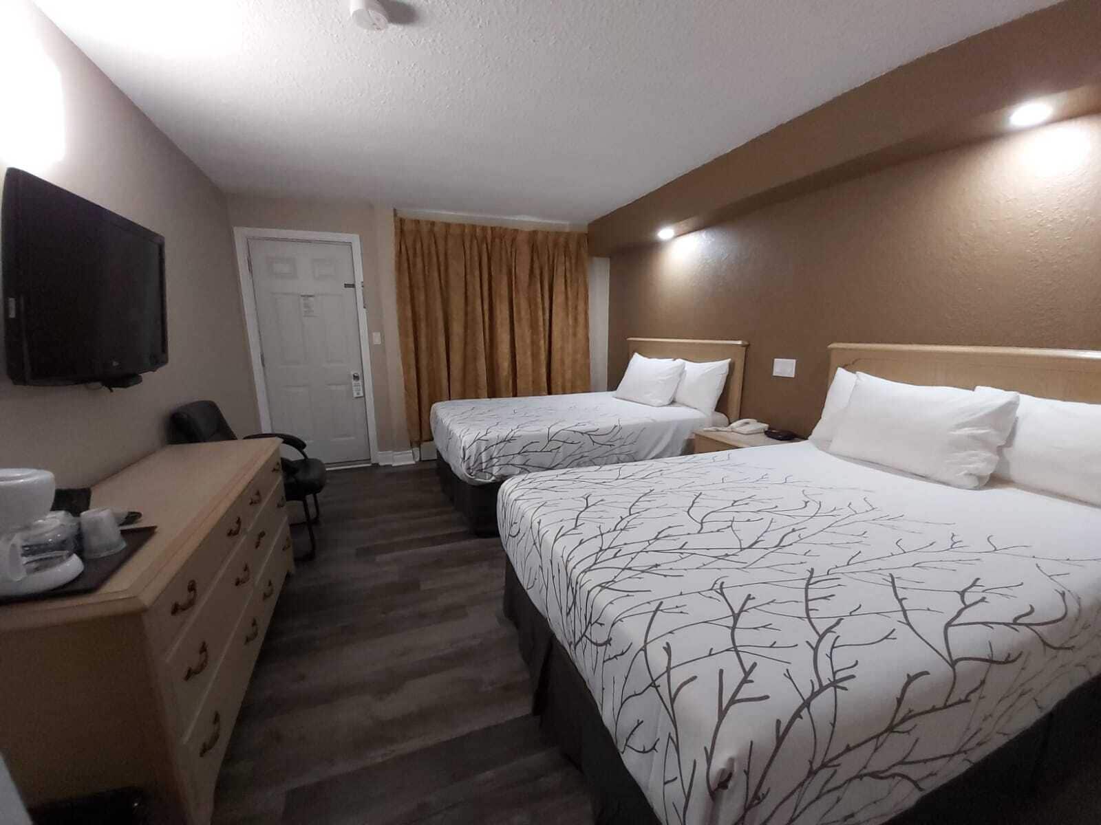 Una habitación de hotel con dos camas, un escritorio con una silla, un televisor y una puerta.