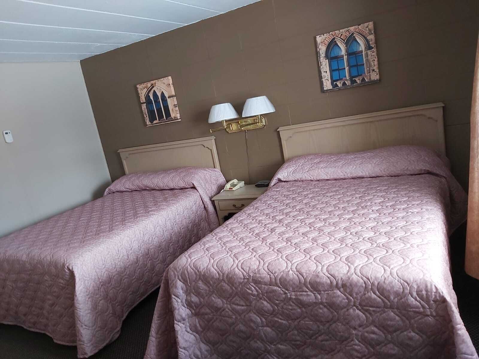 Une chambre d’hôtel avec deux lits, une table de chevet avec une lampe et deux cadres photos accrochés au mur.