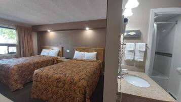 Habitación de hotel con dos camas, baño con lavamanos y espejo, y ducha.